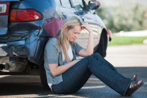 An injured woman sits beside her car, waiting for her Islip car accident lawyer.